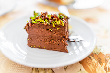 Fototapeta na wymiar Closeup macro view of homemade layered pistachio chocolate raw vegan cake slice on white plate with chocolate shavings and nut green pieces texture