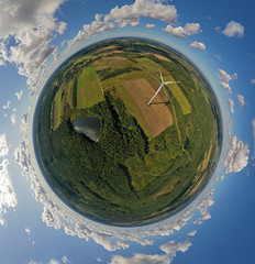 Aerial drone 360 degree view on wind turbine, snake shape road, wheat fields and forest during summer