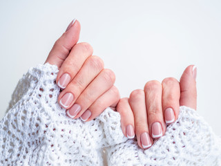 Female hands in cozy knitted sweater demonstrate fingernails with natural color nail polish and...