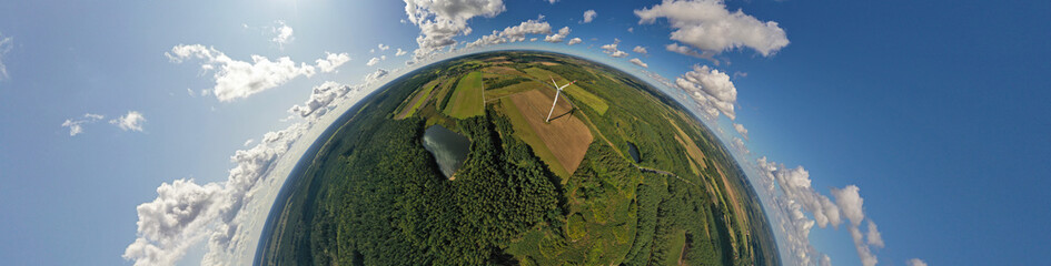 Aerial drone 180 degree arch view on wind turbine, snake shape road, wheat fields and forest during summer
