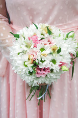 Stylish bride in a white dress holds an unusual wedding bouquet close-up. Delicate wedding bouquet of different flowers in the hands of the bride, selective focus.