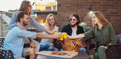 Youngsters spend spare time on a loft terrace with beer, pizza and guitar