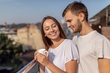 Young cute couple enjoys the view while having coffee on a summer balcony