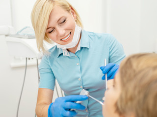 Smiling female dentist in blue scrubs using water spray syringe