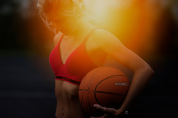 Fototapeta premium Portrait of a gorgeous concentrated beautiful strong athletic woman outdoors posing while listening to music with headphones holding a basketball.healthy lifestyle concept, sporty girl