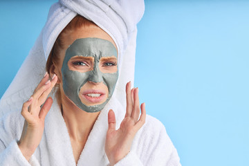 Female with perfect skin and natural make-up. Wearing bathrobe and towel after bathing, using mask. Isolated over blue background