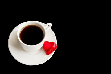 Cup of coffee with heart shaped candy isolated on black background 