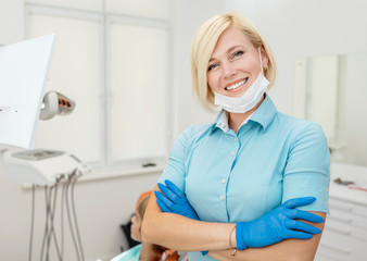 Portrait of cute blonde dentist in blue scrubs and gloves posing in her workplace