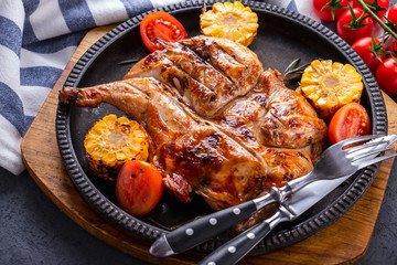 Delicious roasted small  chicken  with corn and tomatoes on frying pan. Closeup