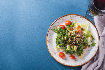 Arugula salad with cherry tomatoes and pine nuts in plate. Top view. Copyspace