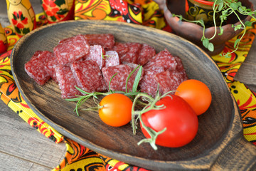 Dry salami sausage sliced ​​on a wooden board and covered with spices, tomatoes. Russian cuisine