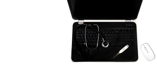 Concept: diagnostics, laptop and computer repair. A silver stethoscope lying on a black laptop, next to it is a thermometer that shows the temperature 98.6. Near the laptop is a white mouse PC