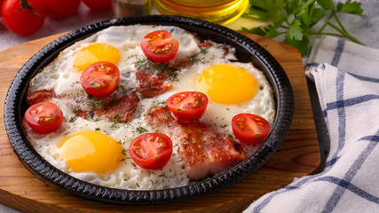 Fried eggs, bacon and tomatoes on a frying pan. Breakfast concept
