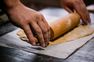 baker's hands roll ginger dough on a dark background. Close-up, soft focus. Side view, top view. Copy space.