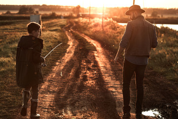 Father and son walk along country road along lake to fishing spot. Sunset.