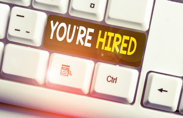 Conceptual hand writing showing You Re Hired. Concept meaning New Job Employed Newbie Enlisted Accepted Recruited White pc keyboard with note paper above the white background