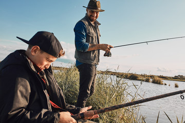 Happy caucasian father and son fish together near lake. This is first fishing for boy. He fun and happy. Warm sunny day.