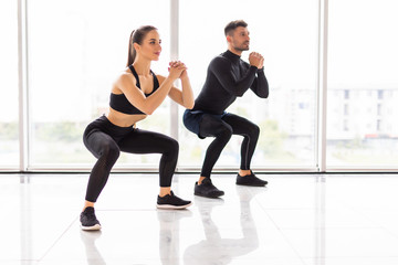 Deep squat. Fitness couple in sportswear doing squat exercises at gym