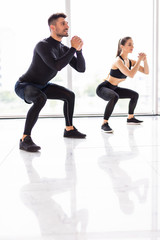 Fototapeta na wymiar Deep squat. Fitness couple in sportswear doing squat exercises at gym