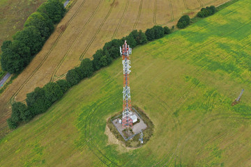 Aerial drone perspective view on high telecommunication steel tower placed in rural area surrounded by meadows, forest and wheat fields