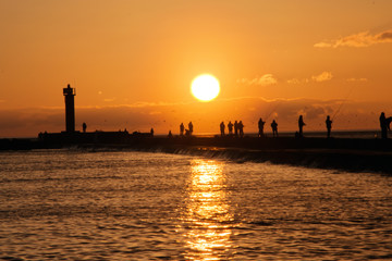 Sunset view with silhouettes of people fishing at baltic sea on Mangalsala pier in Riga
