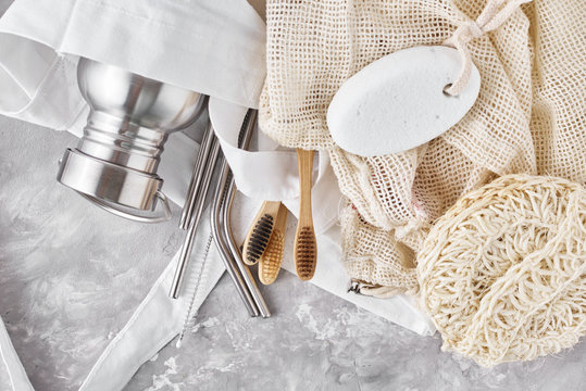 Zero Waste Concept. Eco Friendly Reusable Items In Natural Shopping Bag. Bamboo Toothbrushes, Spongle, Aluminum Bottle And Metal Tubes On A Gray Background.