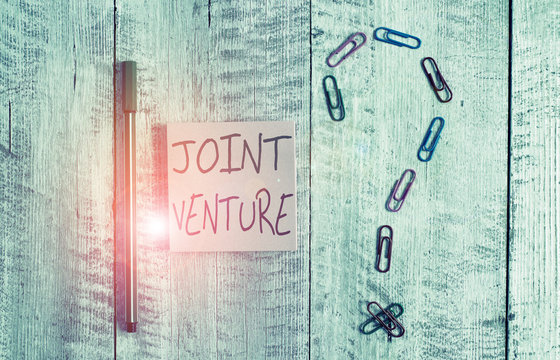 Word writing text Joint Venture. Business photo showcasing Collaboration Arrangement Parties Partnership Team Pastel colour note paper placed next to stationary above the wooden table