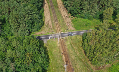 Aerial drone perspective view on railroad crossing with asphalt road in the forest with car passing