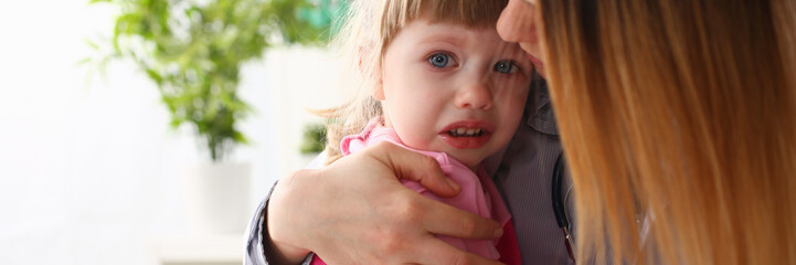Doctor hugging scared crying little baby girl visiting her office