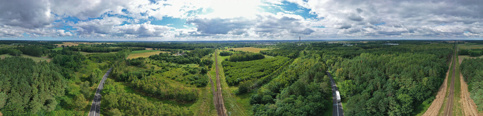 Fototapeta na wymiar Aerial drone wide panoramic view on straight and curved railroad and asphalt road in natural scenery with green forest, cargo truck on the way.