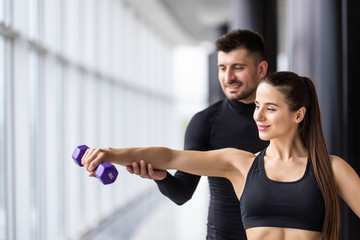Attractive woman and a personal trainer with weight training at gym