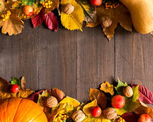 Dynie z liśćmi, orzechami, jarzębiną i darami jesieni na drewnianym tle, miejsce na napis  © Nicole
