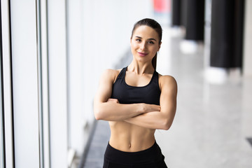 Fototapeta na wymiar Smiling sports woman standing with arms folded and looking at camera at gym
