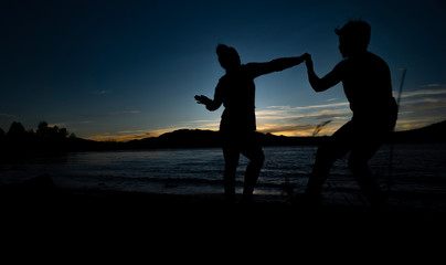 Fototapeta na wymiar silhouette of couple dancing during sunset next to lake DIGITAL CAMERA
