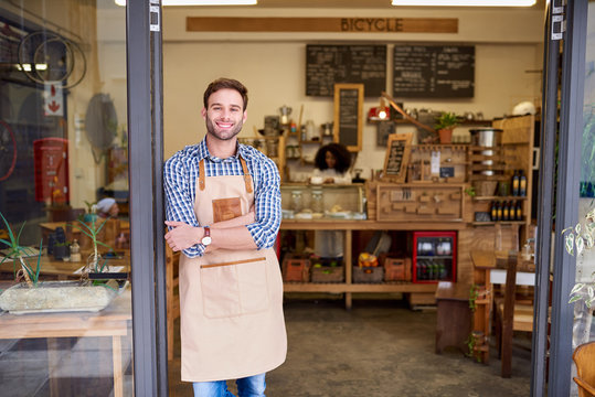 Smiling Young Barista Standing At The Entrance Of A Cafe