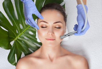The cosmetologist makes the  Microdermabrasion procedure of the facial skin of a woman in a beauty...