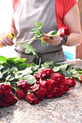 Fototapeta na wymiar Florist collects a bouquet. Woman is cleaning roses on table.