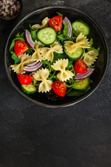 italian pasta salad farfalle, vegetables, mix leaves (tomato, cucumber, onion, lettuce, chard, arugula and more) menu concept. food background. copy space. Top view