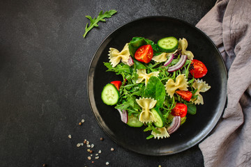 italian pasta salad farfalle, vegetables, mix leaves (tomato, cucumber, onion, lettuce, chard, arugula and more) menu concept. food background. copy space. Top view