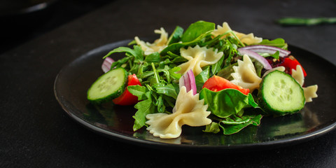 italian pasta salad farfalle, vegetables, mix leaves (tomato, cucumber, onion, lettuce, chard, arugula and more) menu concept. food background. copy space. Top view