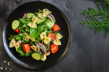 italian pasta salad farfalle, vegetables, mix leaves (tomato, cucumber, onion, lettuce, chard, arugula and more) menu concept. food background. copy space. Top view