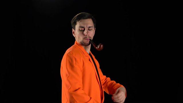 Man in a bright suit stands and smokes with a pipe gazing intently at the camera