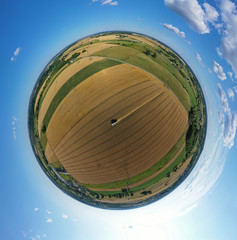 Aerial drone 360 degree panoramic view on harvester cutting wheat field in surrounding of forest and village.