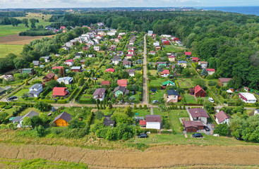 Aerial perspective drone view on allotment gardens with high density of houses in forest, sea and agricultural fields surroundings