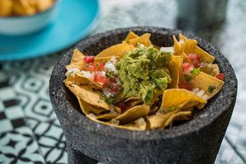 Yellow corn nacho chips garnished with ground beef, guacamole, melted cheese, peppers and cilantro leaves a molcajete, traditional Mexican mortar.
