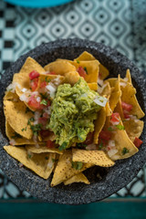 Yellow corn nacho chips garnished with ground beef, guacamole, melted cheese, peppers and cilantro leaves a molcajete, traditional Mexican mortar.