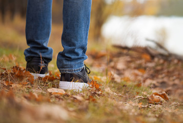 Men's feet in stylish black sneakers in autumn Park or forest. Seasonal shoes