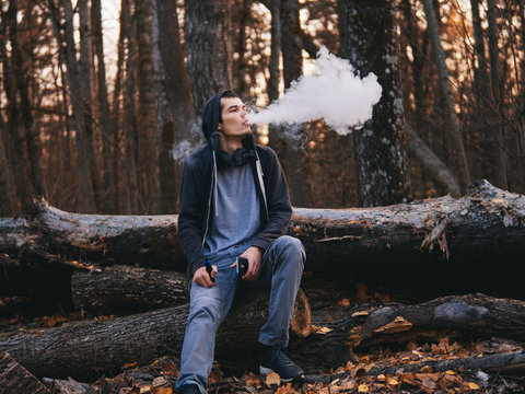 a male vaper in an autumn Park exhales a large cloud of smoke or steam