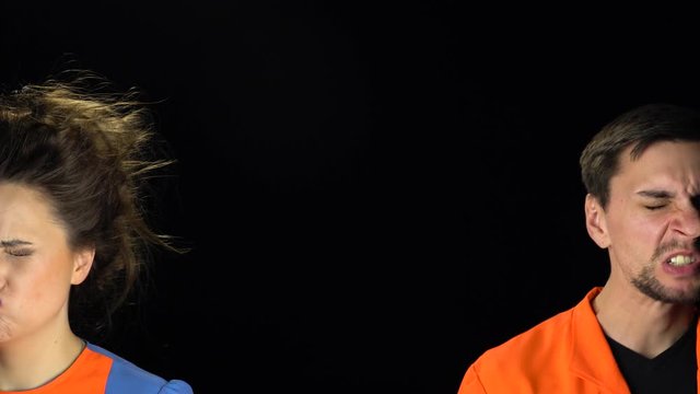 Guy and a girl are looking at the camera making grimaces with copy space between them at black background