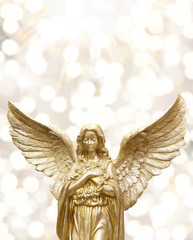 Golden shiny angle statue against a bright bokeh background.